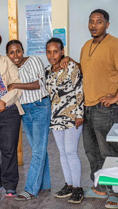 A sponsored youth, Eyuel, stands with women of the sewing program.