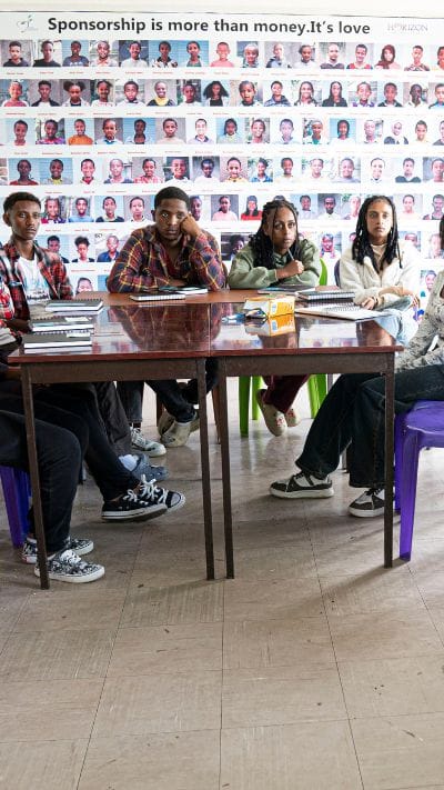 Collaborative Ventures students sit together in a training classroom, with a wall of sponsored student portraits behind them.