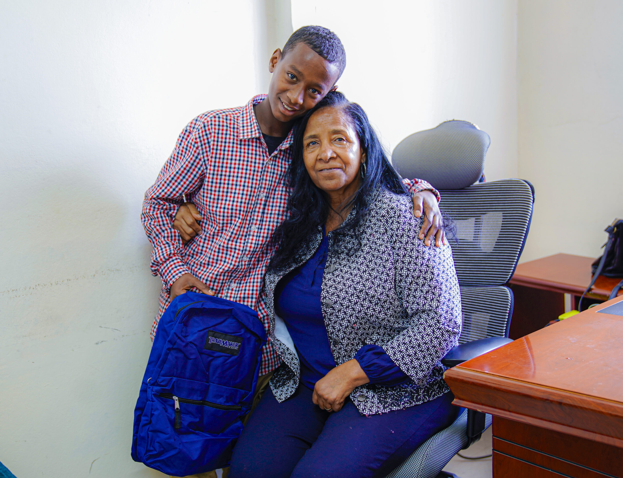LCE founder Mulu smiling warmly while embracing a young sponsored student holding his new school backpack.