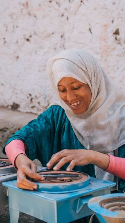 A widow, Nurit, in the Widow Empowerment Program smiles while assembling a traditional Ethiopian mitad at her workshop.