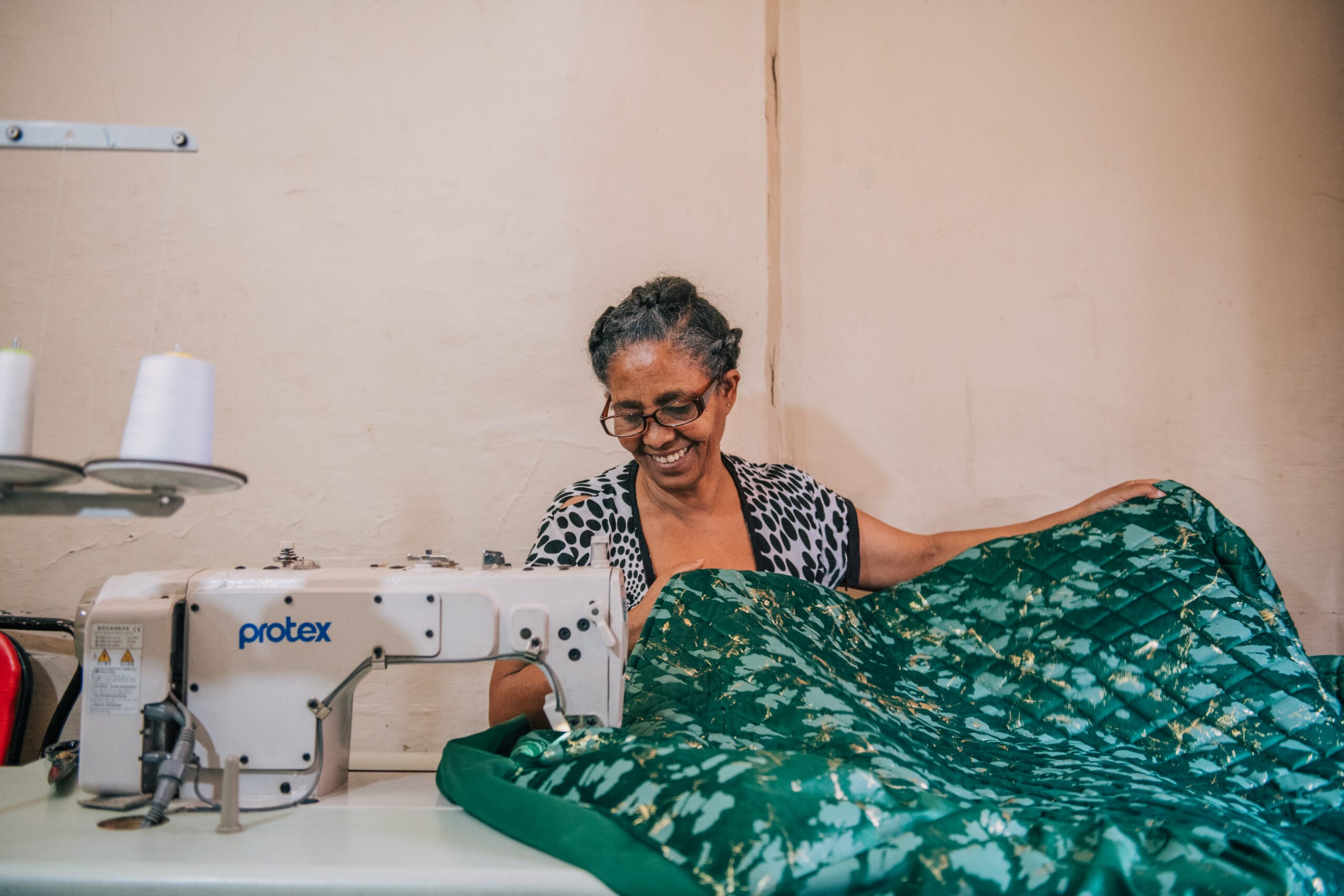 A smiling Ethiopian woman operating a professional sewing machine to tailor garments for her independent, widow-owned business.